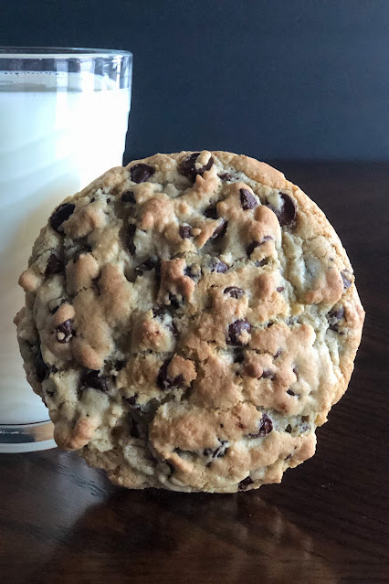 large chocolate chip cookie in front of a glass of milk