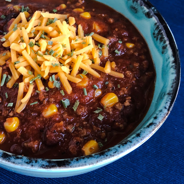 sweet corn & black bean chili in a turquoise bowl with cheese on top