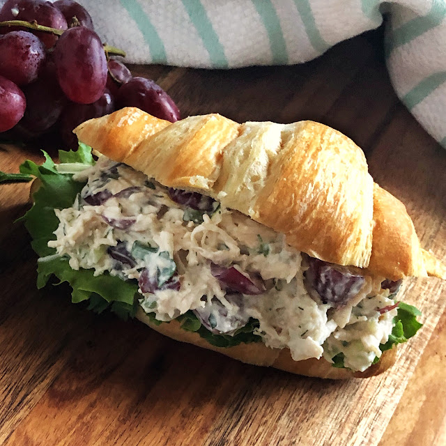 chicken salad on a croissant with a bunch of grapes