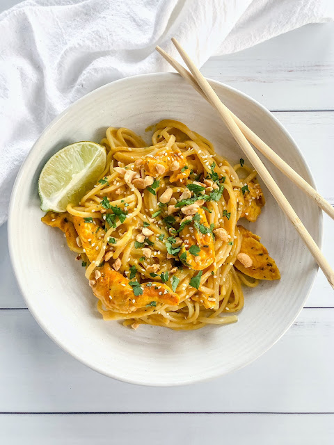 chicken and noodles on a white plate with a lime and chopsticks