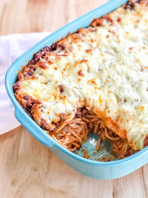 spaghetti casserole smothered in cheese in a teal baking dish