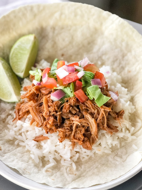 sweet shredded pork with white rice and pico de gallo on a white tortilla with limes