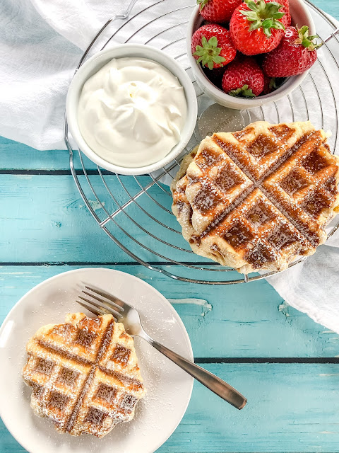 waffles cream and strawberries on a cooling rack and a white plate with a waffle and fork on the side