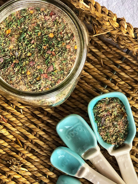 herbs and spices in a jar with a spoon next to it