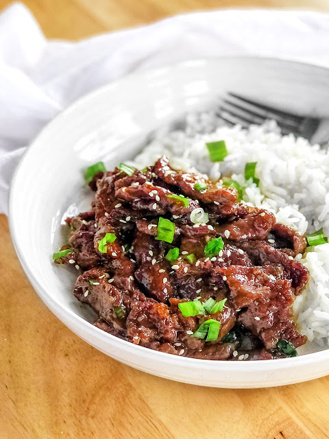 mongolian beef with rice, spring onions and sesame seeds on a white plate