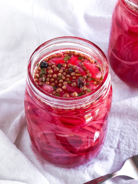 red onions and spices in pink vinegar in a quart jar