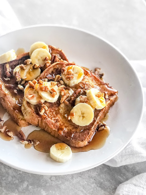 french toast with pecans bananas and syrup on a white plate