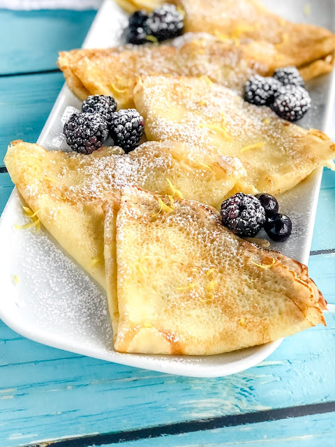 folded crepes on a white plate with berries and lemon zest
