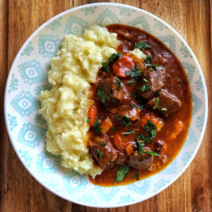 Beef Bourguignon over mashed potatoes on a blue and white plate