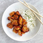 sweet and sour chicken with rice on a white plate with chopsticks