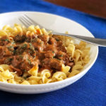 goulash stew with egg noodles in a white bowl