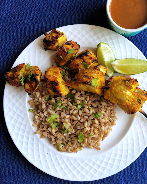 farro with chicken skewers on a white plate with wedges of lime and sauce on the side