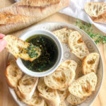 green herbs and garlic with olive oil and balsamic in a small white bowl with crusty bread on the side