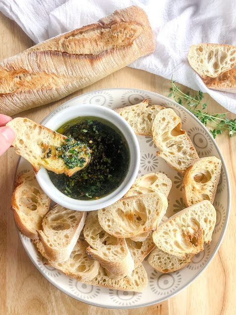 green herbs and garlic with olive oil and balsamic in a small white bowl with crusty bread on the side