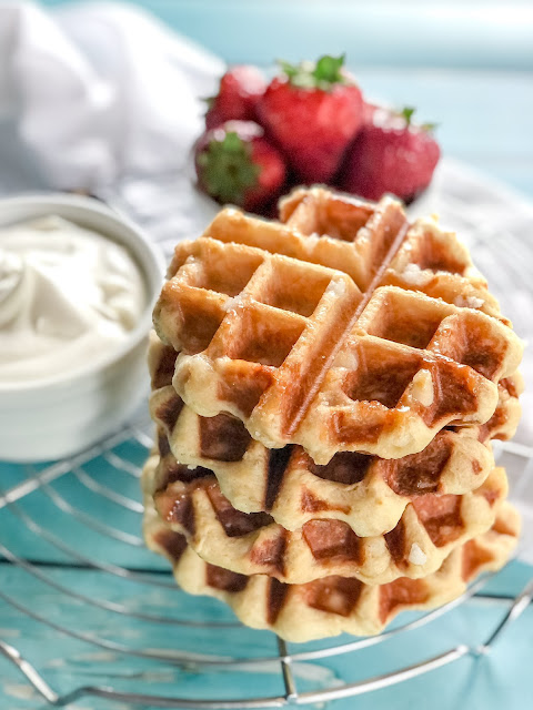 stacked waffles on a cooling rack with whipped cream and strawberries on the side