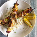 chicken skewers over rice with lemon wedges on a white plate