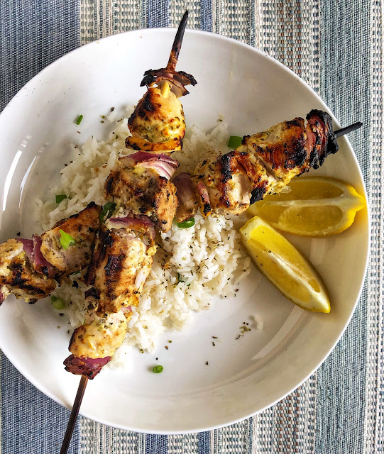 chicken skewers over rice with lemon wedges on a white plate