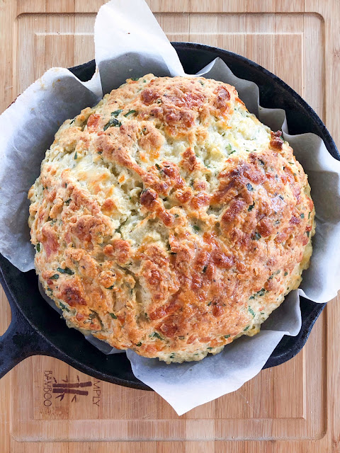 a round loaf of cheese herb bread in a cast iron pan