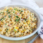 pasta salad with corn bacon cheese and parsley in a white bowl with a spoon