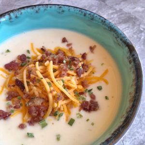 soup in a blue bowl with bacon cheese and chives on top