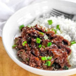 mongolian beef with rice, spring onions and sesame seeds on a white plate