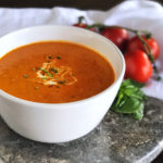 Roasted Tomato Soup in a white bowl garnished with cream and herbs