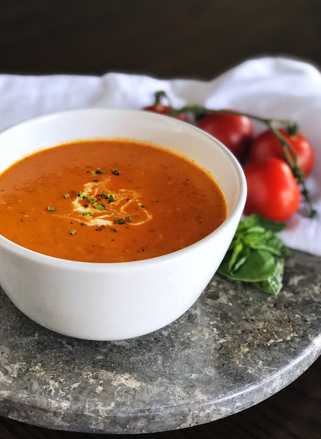 Roasted Tomato Soup in a white bowl garnished with cream and herbs