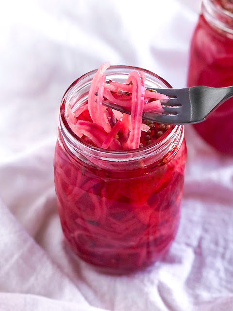 red onions in pink vinegar in a quart jar with a fork