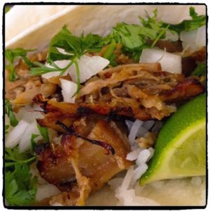 pork carnitas with onion cilantro and lime over a tortilla and rice