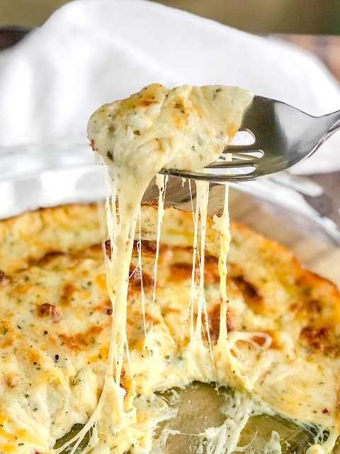 a spoon of melted cheese dripping in to a pie dish full of melted cheese
