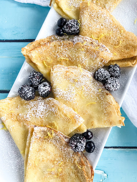 crepes folded on a white dish with berries and lemon zest