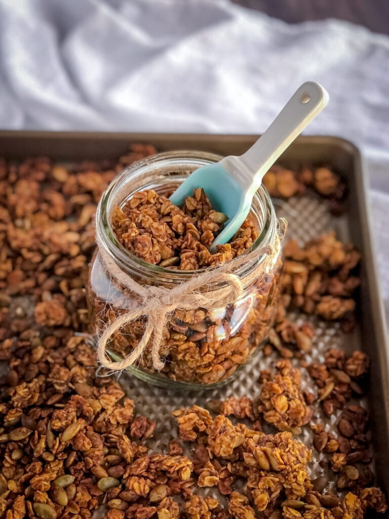 granola in a jar with a spoon on a baking sheet