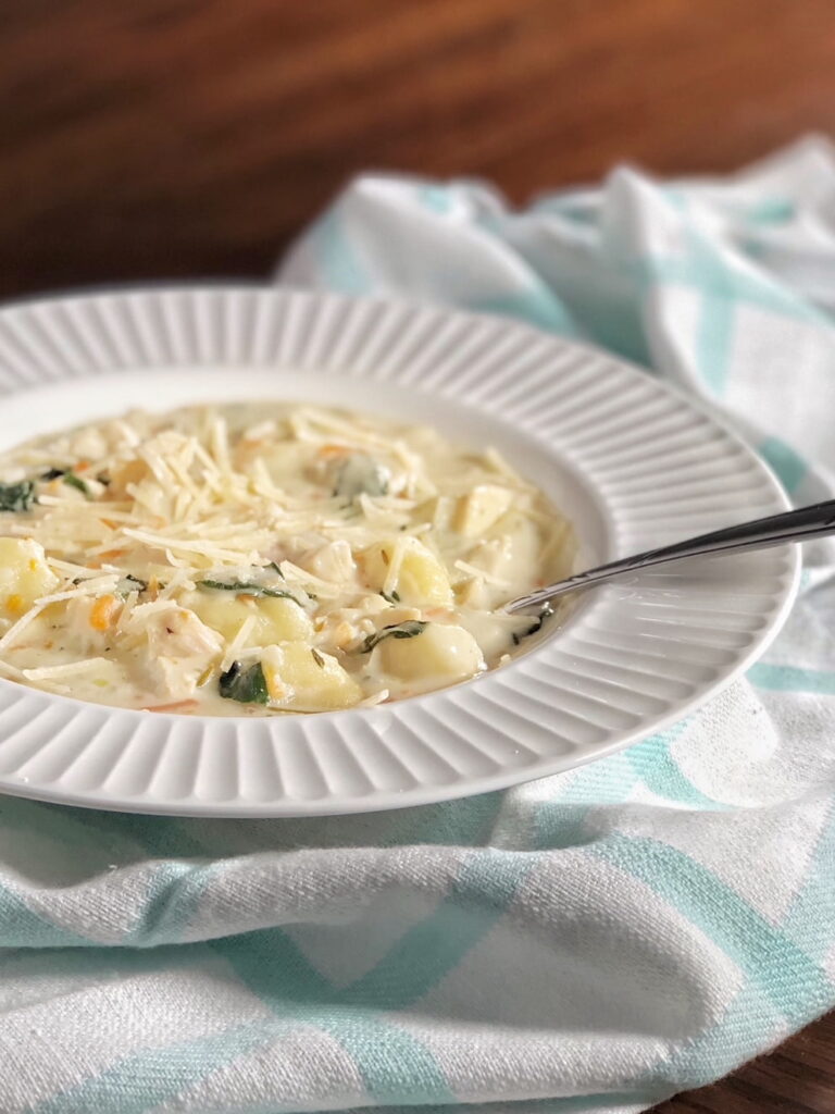 chicken gnocchi soup in a white bowl with a spoon