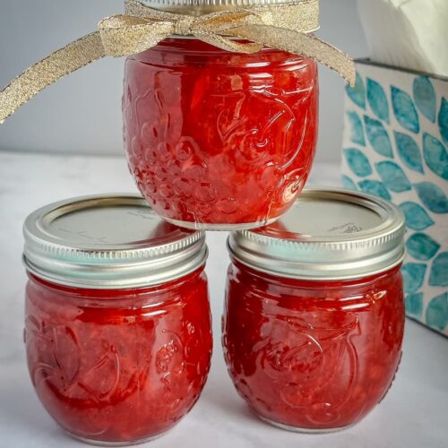A small batch of homemade strawberry jam in glass jars, filled with bright red jam made from fresh strawberries, on a kitchen counter.
