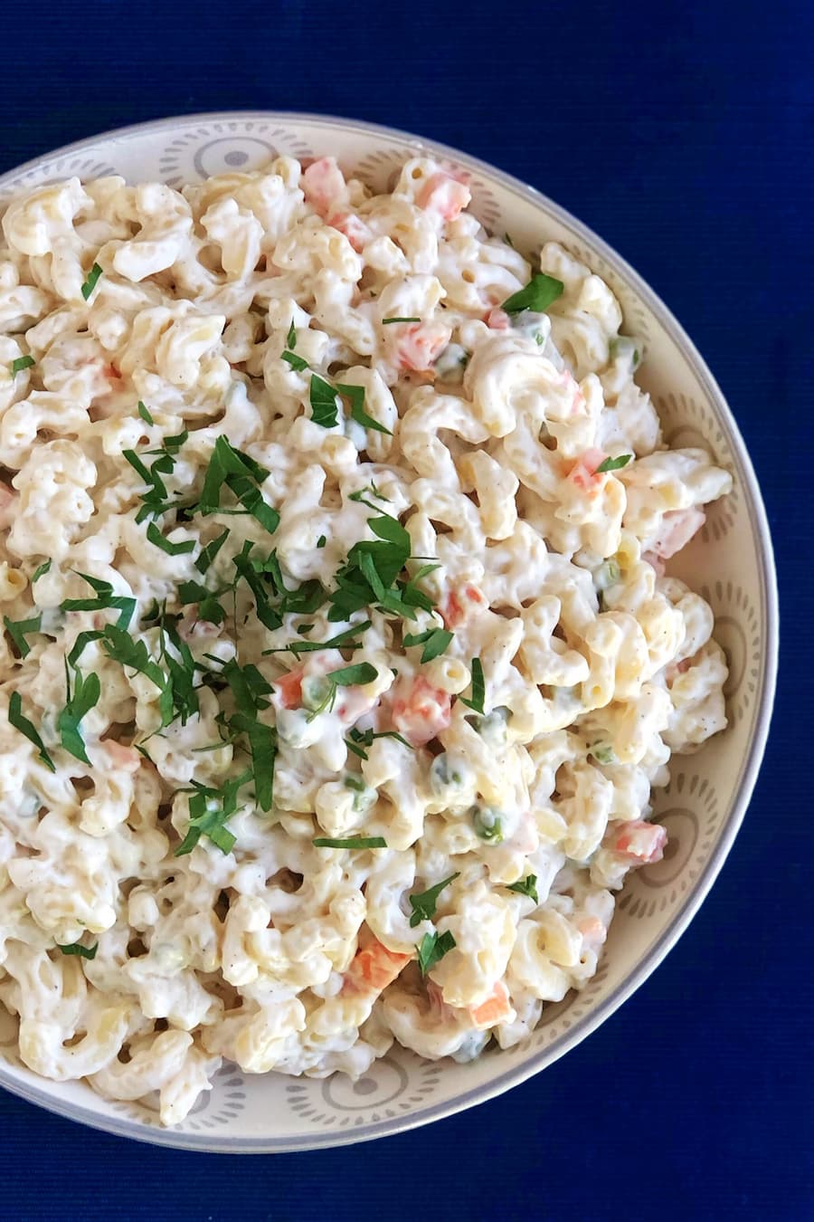Creamy Hawaiian macaroni salad with peas, carrots, and shredded red onion in a white bowl, garnished with parsley.